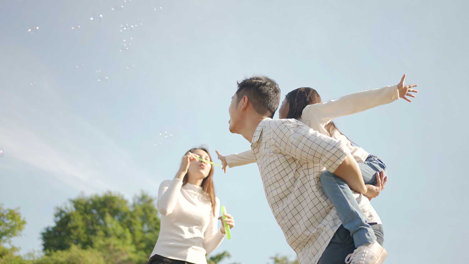 happy young asian father piggyback with his little girl while mother run play with her park enjoyed ourselves together green garden family enjoying sunny fall day nature