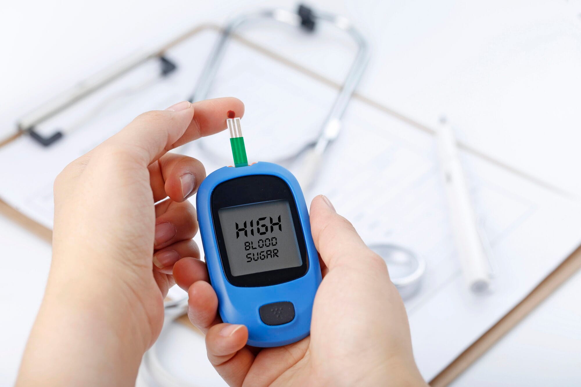 Hand holding a blood glucose meter measuring blood sugar, the background is a stethoscope and chart file NUVIV ดูแลเบาหวานติดเชื้อและเสริมภูมิคุ้มกัน